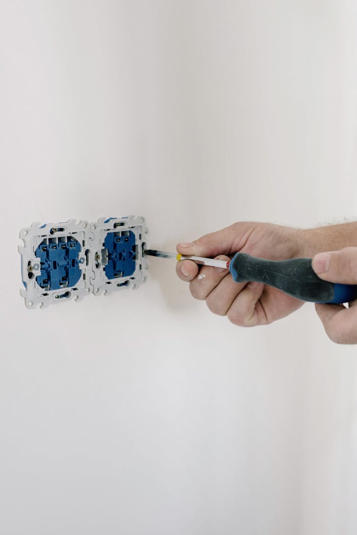 Close-up of hands using a screwdriver to install electrical sockets on a white wall.