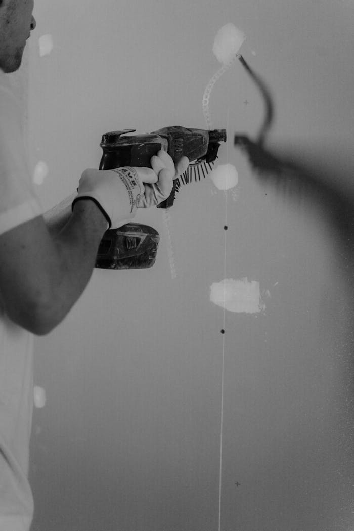 Black-and-white photo of a carpenter using a hand drill on a drywall.